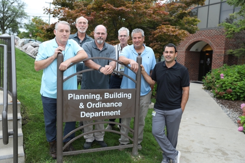 Six men with Building Inspection team standing behind Planning, Building & Ordinance Department sign outside entrance to PBO offices at Township Hall