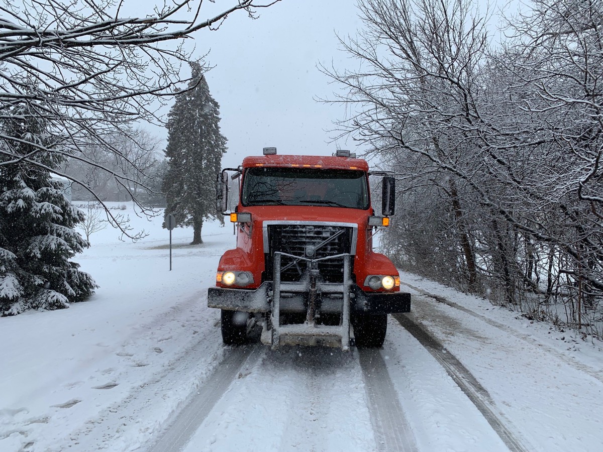 red truck coming towards camera driving down a snowy street surrounded by snowy trees.