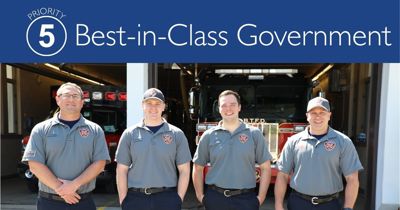 Four firefighters standing in front of the fire station with fire trucks parked inside. Title of Priority 5: Best-in-Class Government