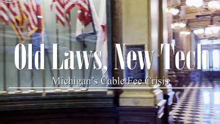 Video Title: Old Laws, New Tech: Michigan's Cable Fee Crisis over what looks to be a government capitol building with American flags in background.