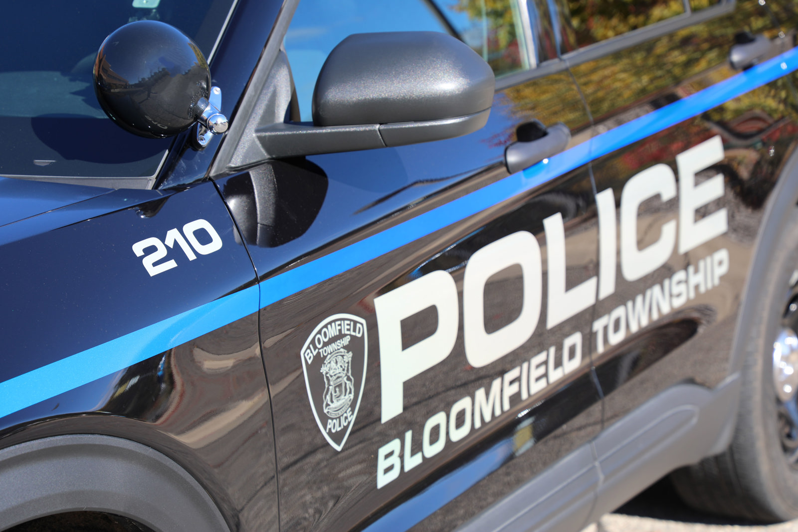 Closeup of the logo and Bloomfield Township Police written on the side of a shiny police vehicle. Green trees and blue sky reflected in the vehicle.